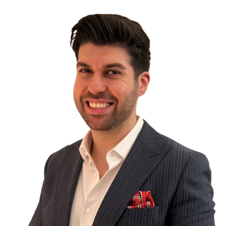 Lächelnder Geschäftsmann im eleganten Nadelstreifenanzug mit weißem Hemd und rotem Einstecktuch, hält eine weiße Kaffeetasse und Untertasse.